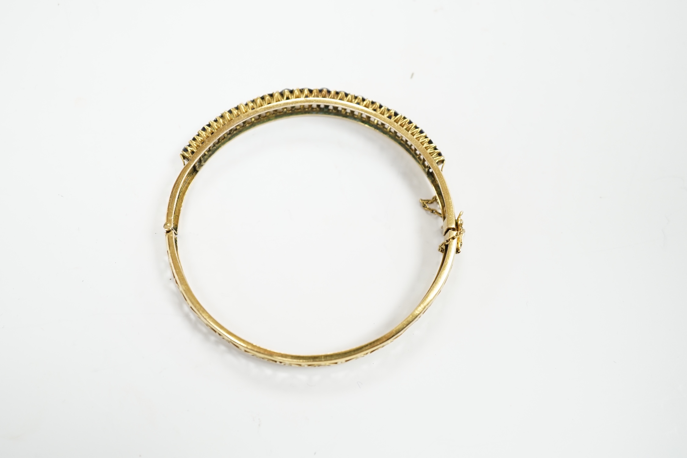A pierced yellow metal and eighteen stone sapphire set hinged bangle, interior diameter 58mm, gross weight 14.1 grams.